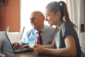 Pflegekraft unterstützt Senior bei der 24-Stunden-Pflege am Computer