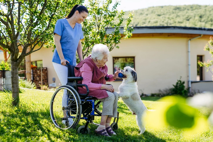 24-Stunden-Pflegedienst: Pflegekraft unterstützt Seniorin im Rollstuhl im Garten